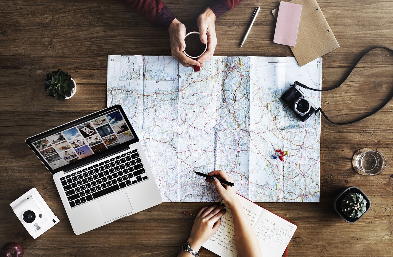 A top-down view of a desk with a travel designer planning the customer next adventure using a laptop and a map.