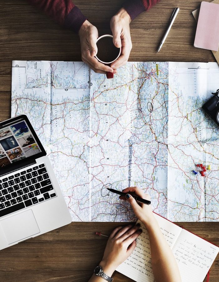 A top-down view of a desk with a travel designer planning the customer next adventure using a laptop and a map.